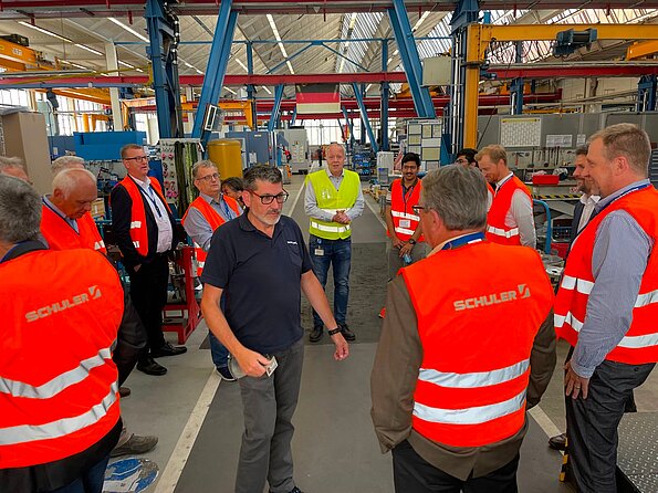 Gruppe von Besuchenden mit Warnwesten bei einer Führung durch eine industrielle Produktionshalle.