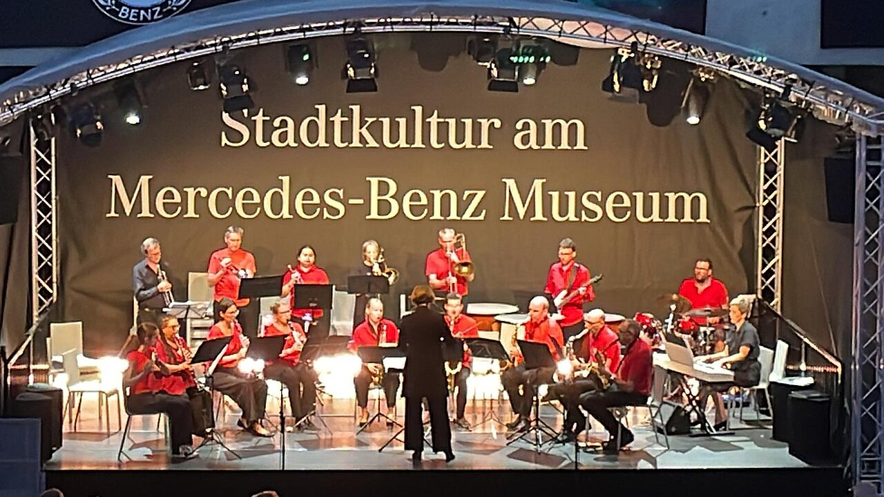 Musikensemble bei einem Konzert auf der Bühne des Mercedes-Benz Museums unter der Überschrift „Stadtkultur am Mercedes-Benz Museum“.