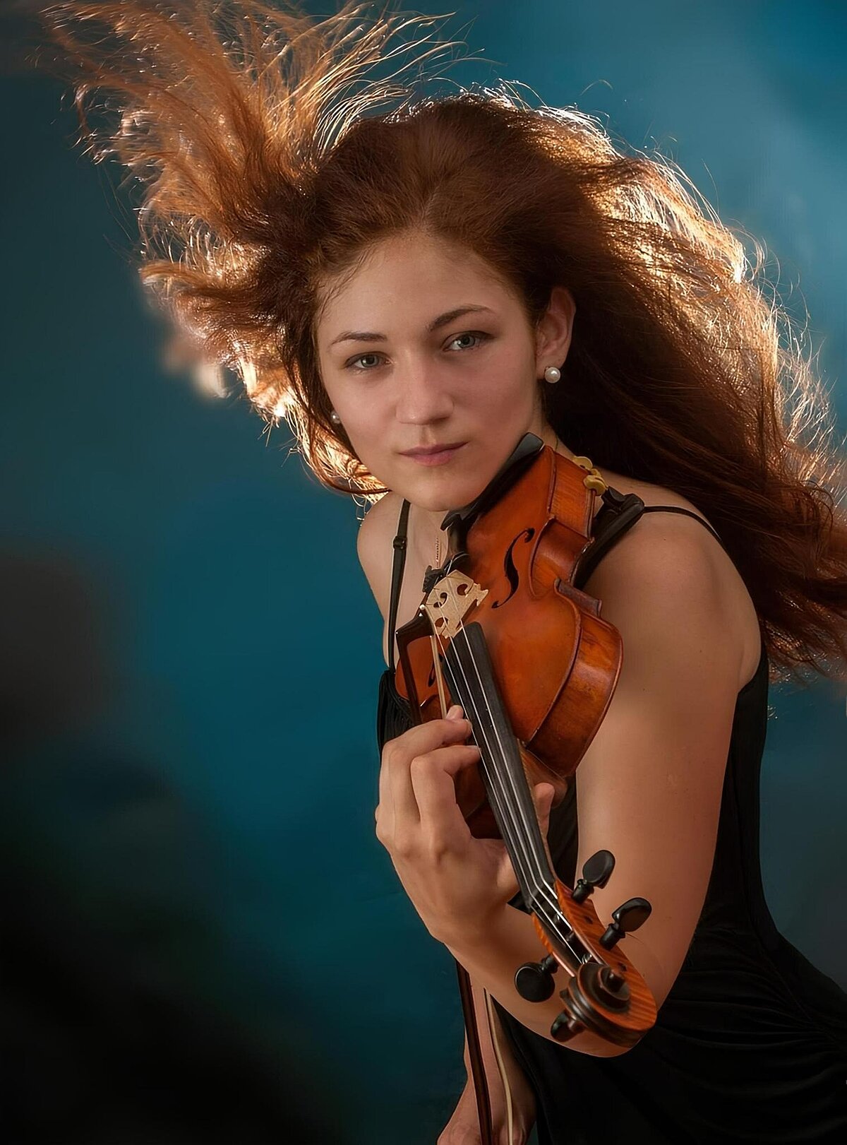 Lebendige Porträtaufnahme vor einem neutralen Hintergrund, von Novikova Oleksandra, die eine Violine spielt.