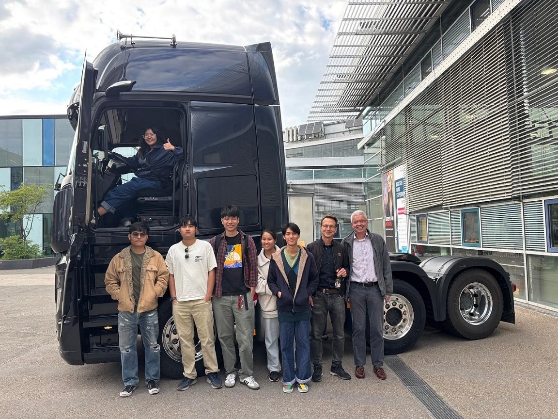 Eine Gruppe thailändischer Studenten steht vor einem großen geparkten Lkw, eine Person sitzt im Fahrerhaus und zeigt einen Daumen nach oben.